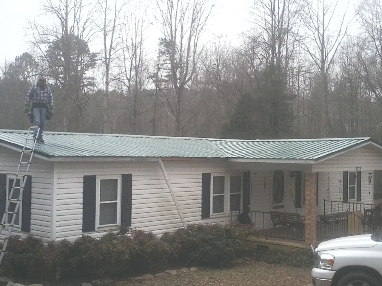 Worker on a ladder beside a new green metal roof on a ranch home in Somerville